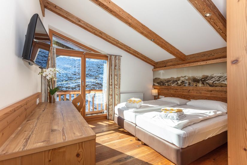 Schlafzimmer der Ferienwohnung 80 mit Doppelbett, sichtbaren Holzbalken, Balkonzugang und Bergblick