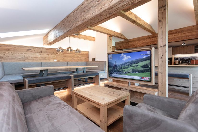 Wohnbereich der Ferienwohnung 80 mit Sofa, Sesseln, Fernseher, großer Sitzecke und sichtbaren Holzbalken