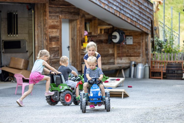 Kinder spielen mit Tretfahrzeugen im Bauernhofurlaub