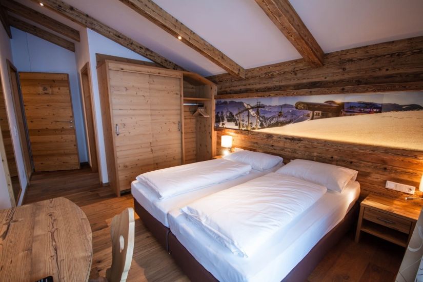 Schlafzimmer der Ferienwohnung 80 mit Doppelbett, Kleiderschrank, sichtbaren Holzbalken und Holzverkleidung