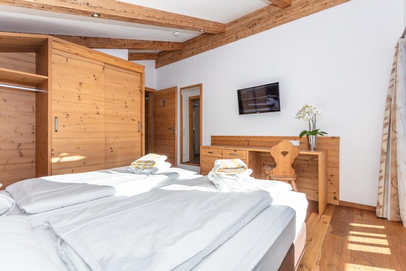 Schlafzimmer der Ferienwohnung 80 mit Doppelbett, Kleiderschrank, Schreibtisch, Fernseher und sichtbaren Holzbalken