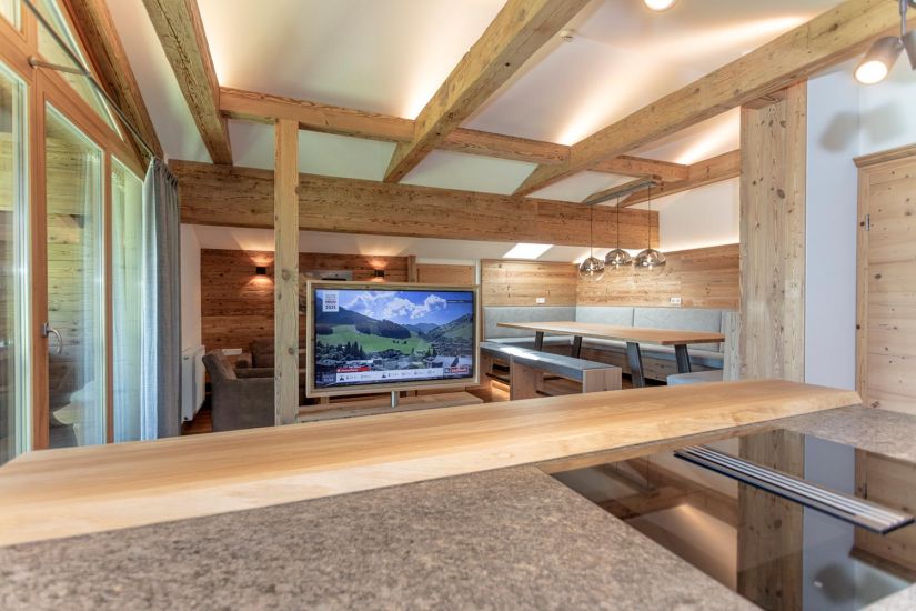 Offener Wohn- und Essbereich der Ferienwohnung 80 mit Sitzecke, Fernseher, sichtbaren Holzbalken und großer Fensterfront