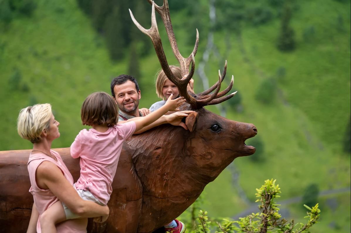 Kinder sitzen auf einem Hirsch - Wildlife Trail im Talschluss von Saalbach Hinterglemm
