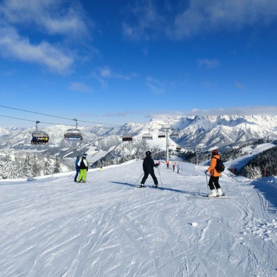 Piste in Saalbach-Hinterglemm mit Skifahrern, Sessellift und den Leoganger Steinbergen im Hintergrund