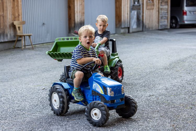 Kinder spielen mit Tretfahrzeugen im Bauernhofurlaub